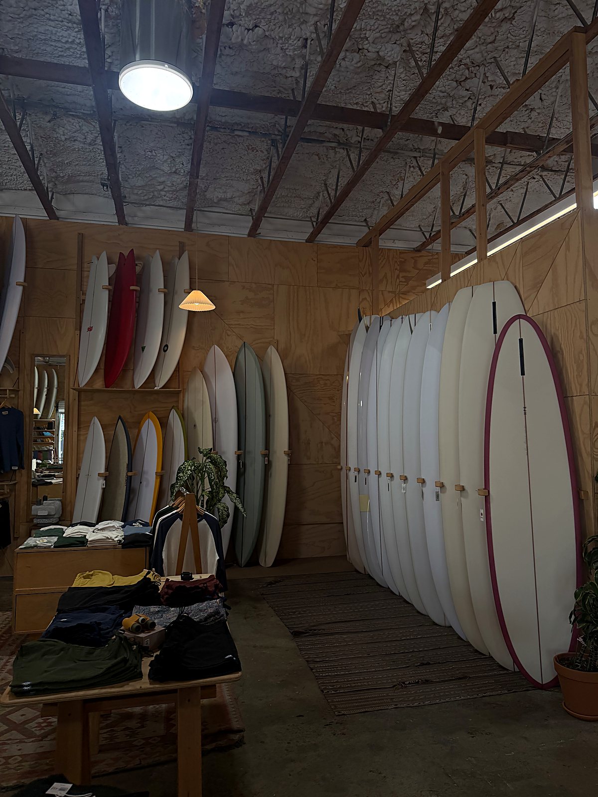 Surfboards lined up along the wall of a wood-framed board shop.