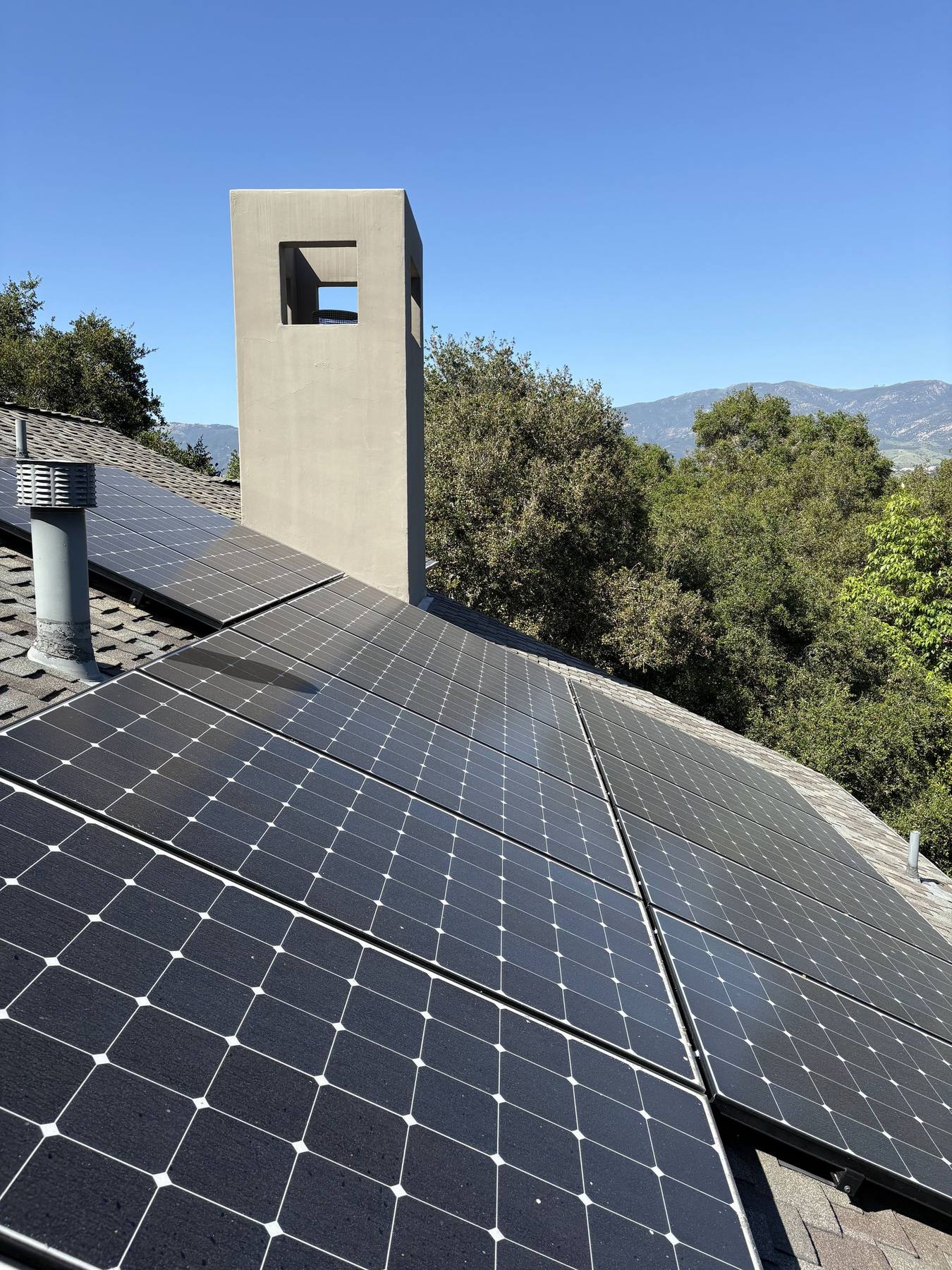 A rooftop solar array dulled by dust and pollen before cleaning, seen past the chimney of a Santa Barbara home.
