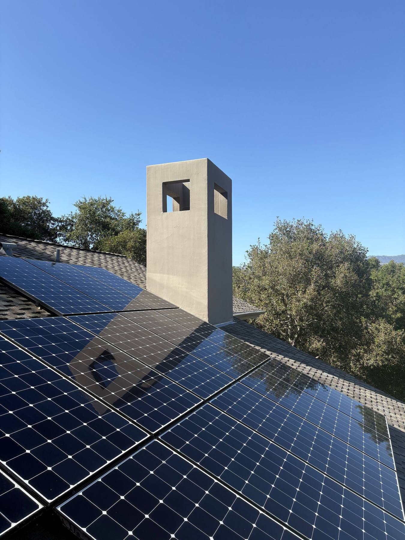 Solar panels beside a modern chimney, clear and reflecting blue sky after cleaning.