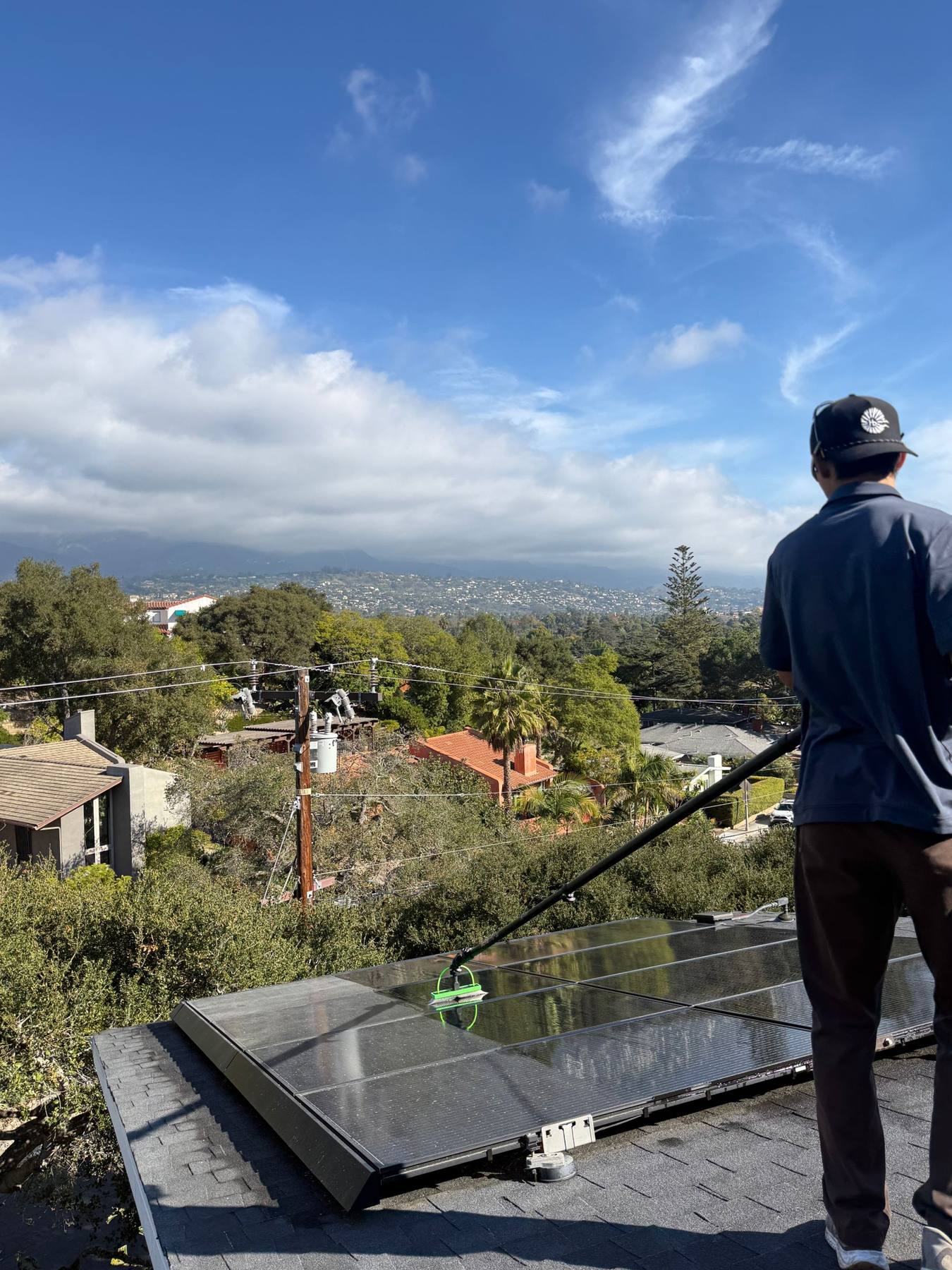 A Lavare technician cleaning a rooftop solar array with a water-fed pole above Santa Barbara.
