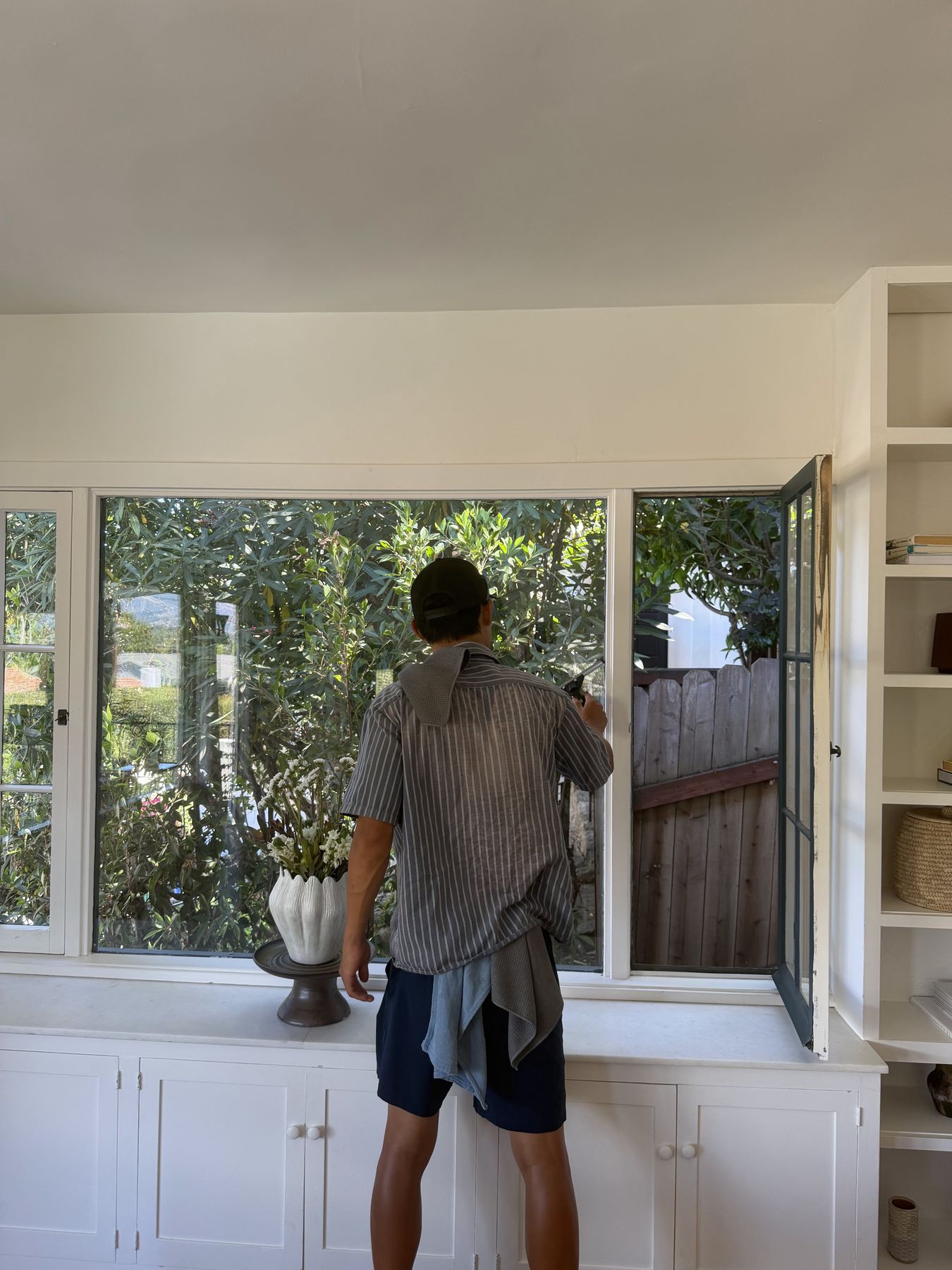 A Lavare window cleaner working on the interior of a bay window above built-in cabinets, garden visible through the glass.