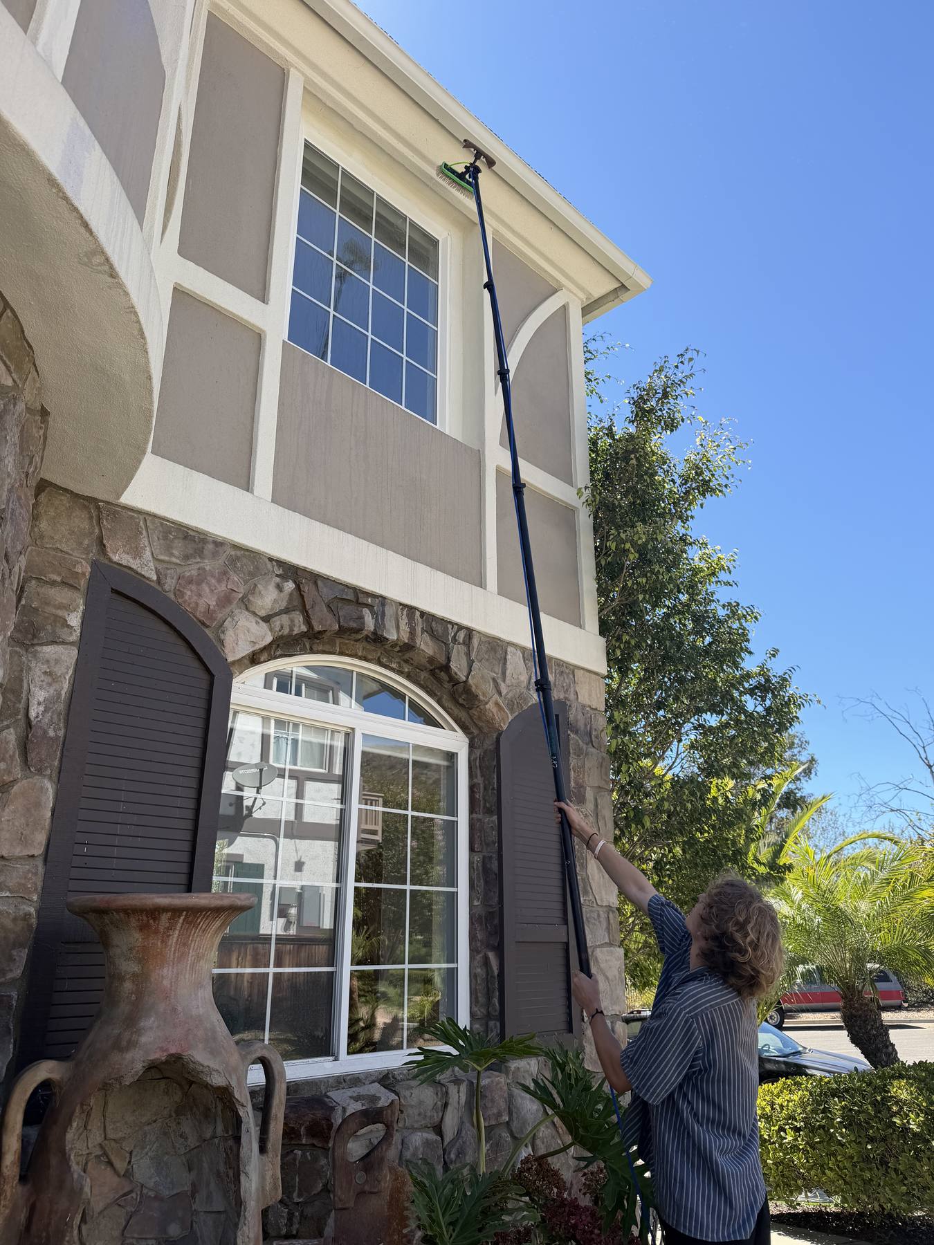 Technician reaching a second-story window with a water-fed pole at a Santa Barbara estate.